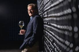 Man in suit holding a glass of wine near a dark backdrop