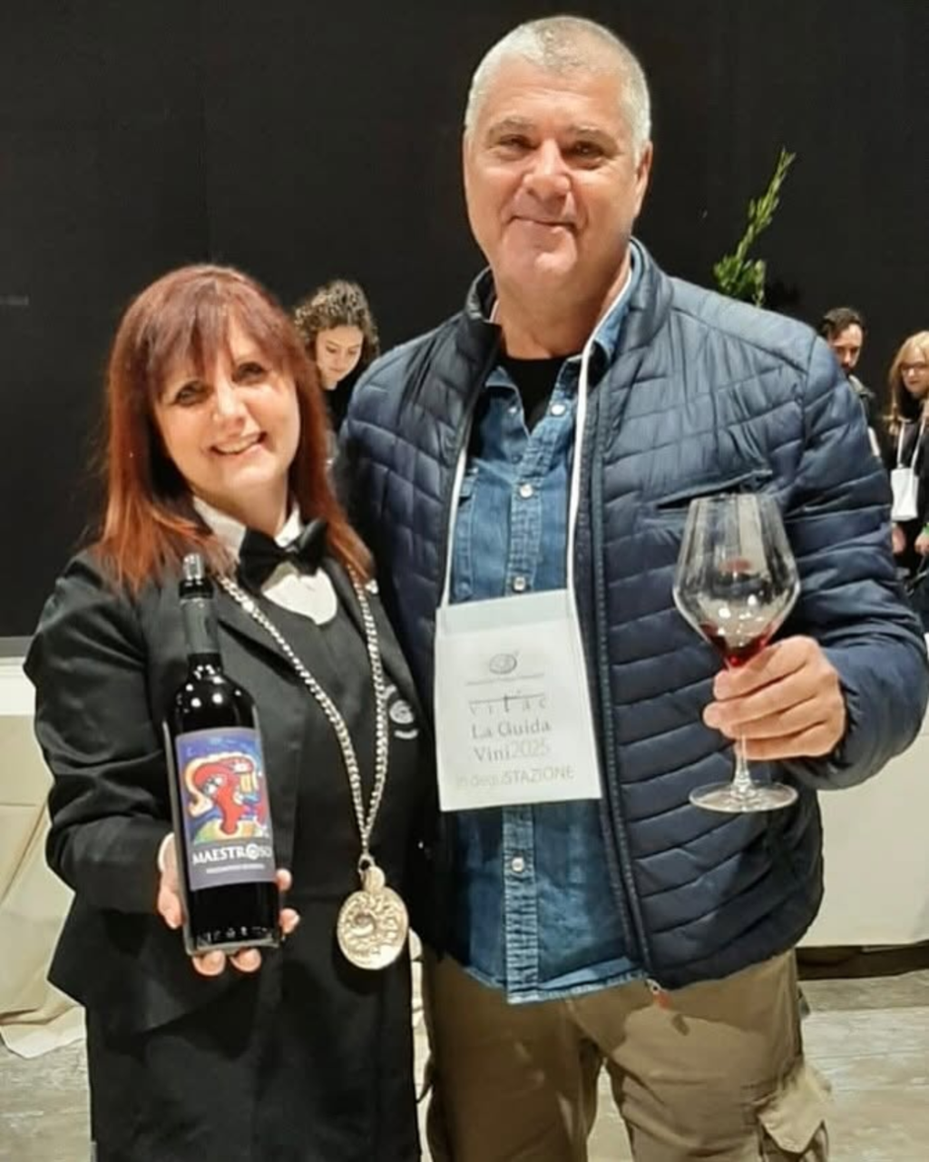 Attendees holding a dark wine bottle and a wine glass at a tasting