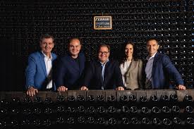 Wine-tasting group of five people standing behind bottles on a table