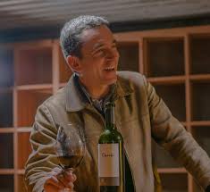 Carmenere red wine bottle held by man in winery with glass nearby
