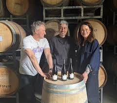 Wine tasting bottles and glasses on a barrel with three people nearby