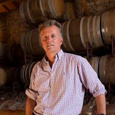 Winery worker standing among wooden barrels, light check shirt, hands on hips