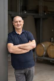 Winemaker standing with arms crossed in front of winery building