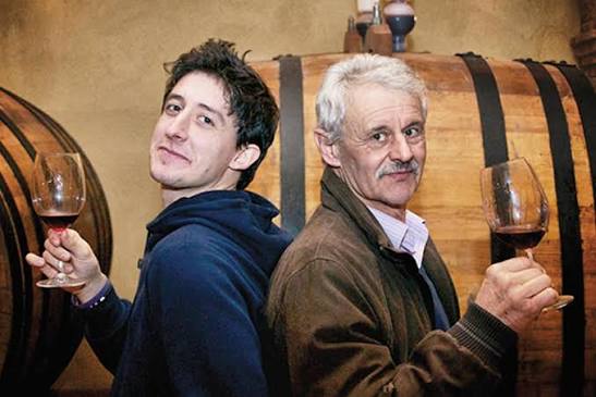 Two men holding wine glasses by wooden barrels during Barolo tasting
